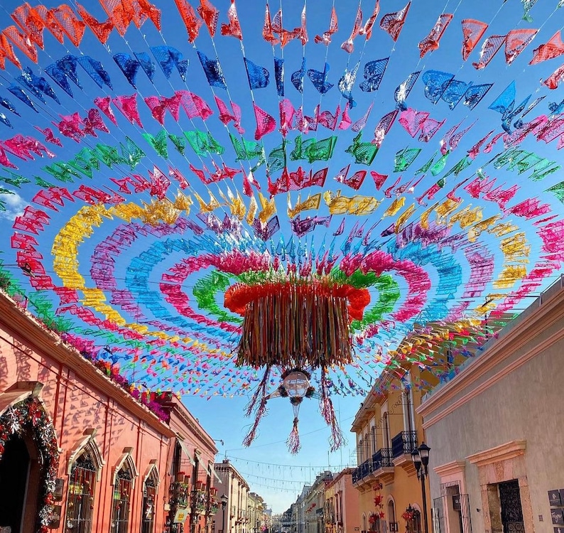 May include: A colorful display of paper flags hanging from a ceiling, creating a festive atmosphere. The flags are in various shades of red, yellow, blue, green, and purple, forming a circular pattern. The flags are strung together with string and are hanging from a ceiling.