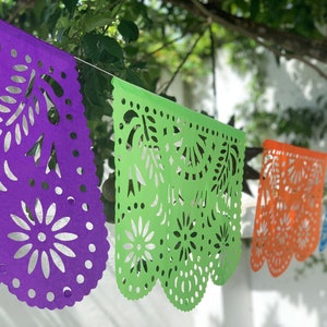 May include: A string of colorful paper banners with intricate cut-out designs. The banners are purple, green, orange, and blue. They are hanging from a string and are strung together in a row.