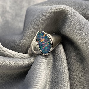 May include: A silver ring with a large oval-shaped opal gemstone. The opal is a vibrant mix of blue, green, and orange.