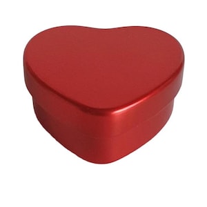 Pode incluir: Uma lata de metal vermelha em forma de coração com um acabamento liso e brilhante. A lata está fechada e tem uma parte superior arredondada.