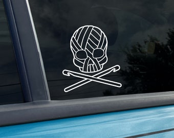 May include: A white vinyl sticker of a skull with yarn wrapped around it and two crossed crochet hooks. The skull is wearing a yarn hat.