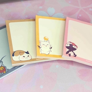 May include: Four different colored memo pads with cartoon characters on them. The pads are stacked on top of each other. The characters are a cat, a bird, a fish, and a creature with wings.