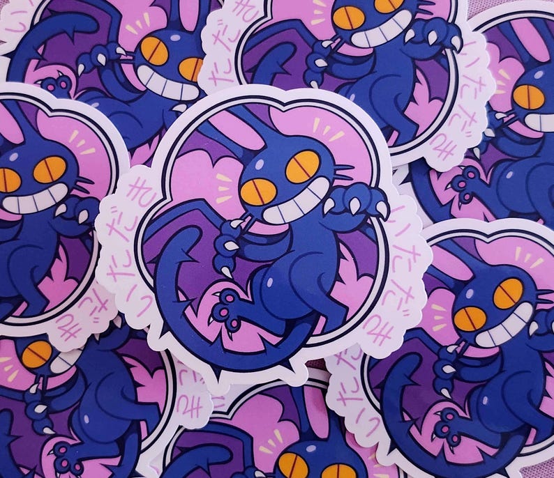 May include: A collection of stickers featuring a cartoonish, dark blue creature with large yellow eyes and a wide grin. The creature has bat-like wings and is set against a pink background with Japanese text. The stickers have a white border.