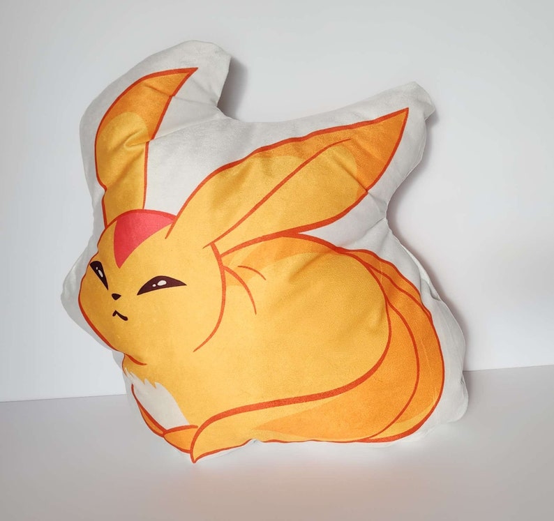 K&ouml;nnte beinhalten: Ein Pl&uuml;schkissen in Form eines gelben und orangefarbenen Fuchses mit einer roten Spitze am Ohr. Der Fuchs hat einen wei&szlig;en Bauch und einen wei&szlig;en Fleck auf der Brust.