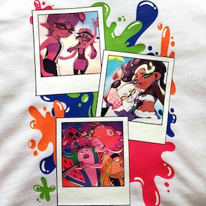 Puede incluir: Una camiseta blanca con un estampado gr&aacute;fico de tres fotos superpuestas al estilo polaroid, rodeadas de salpicaduras de pintura de colores. Las fotos muestran personajes animados en diversos entornos, incluyendo escenas de playa.