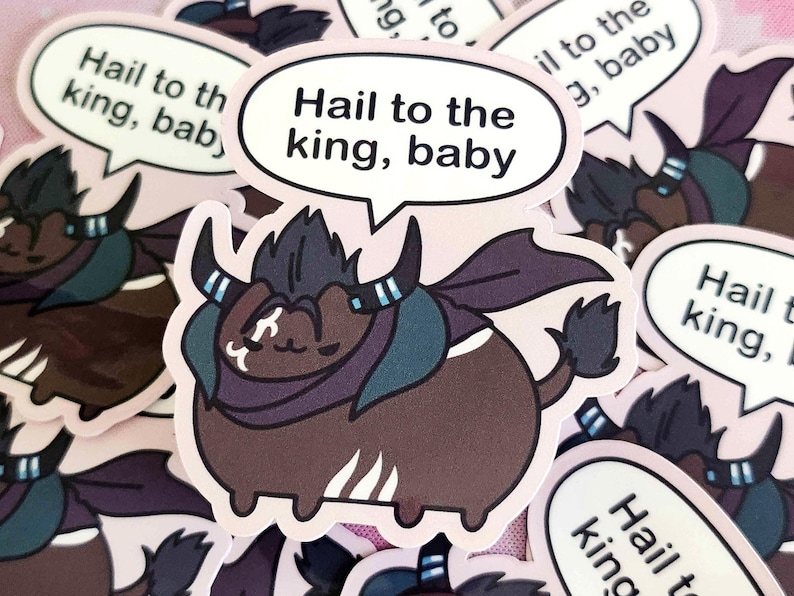 May include: A sticker featuring a cartoon bull with a dark brown body, purple cape, and horns. The bull has a speech bubble that says "Hail to the king, baby" in black text. The sticker is on a pink background.