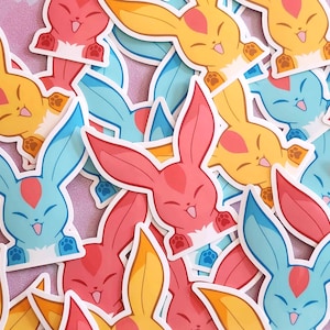 May include: A collection of colorful bunny stickers in shades of pink, yellow, and blue. Each sticker features a cartoon bunny with long ears, a happy expression, and paw prints. The stickers are designed with a white border.