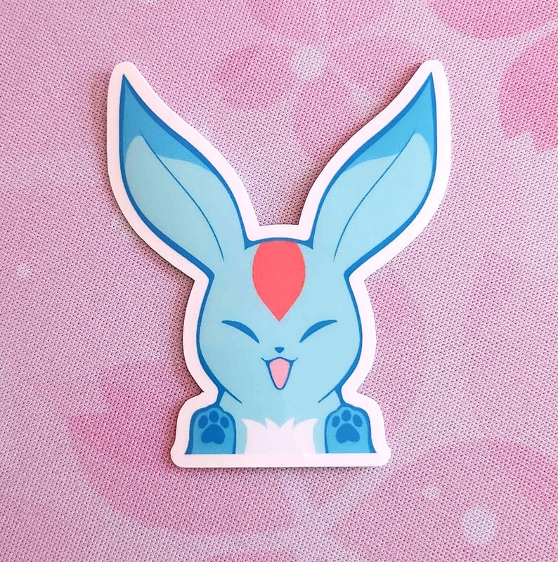 May include: A die-cut sticker featuring a cartoon bunny with large blue ears and a light blue body. The bunny has a red marking on its forehead, a smiling face, and paw prints on its feet. The sticker has a white border.