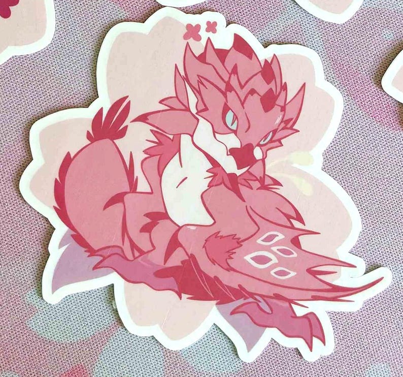 May include: A pink sticker featuring a stylized dragon-like creature with a flower-shaped border. The creature has a detailed design with various shades of pink and white, with a few small stars.