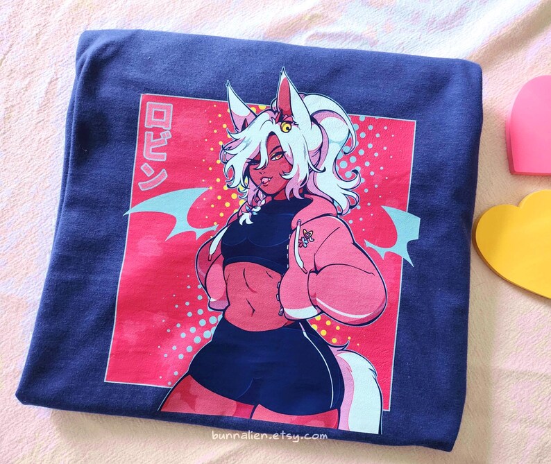 Pu&ograve; includere: Una t-shirt blu navy piegata con un'illustrazione colorata in stile anime. La grafica raffigura un personaggio con capelli bianchi, dettagli rosa e una giacca rosa, su sfondo rosso con testo giapponese. Il nome del negozio Etsy &egrave; visibile.