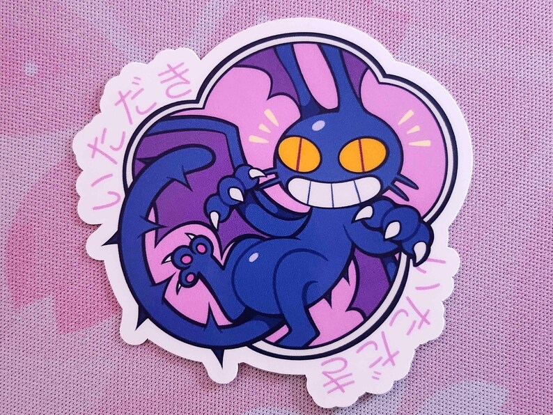 May include: A die-cut sticker featuring a cartoonish blue creature with bat-like wings, a long tail, and sharp claws. The creature has a wide grin, yellow eyes, and is set against a pink and purple background. Japanese text surrounds the image.