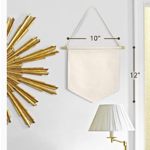 Op de afbeelding: Een blanco canvasbanner met een houten stok aan de bovenkant en een touw om op te hangen. De banner is 25,4 cm breed en 30,5 cm hoog.