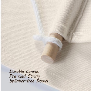 Op de afbeelding: Close-up van een wit canvas met een houten stok en een wit touw. De tekst "Durable Canvas Pre-tied String Splinter-free Dowel" is zichtbaar onderaan de afbeelding.