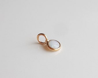 May include: A gold charm with a white opal stone. The charm has a loop for attaching to a necklace or bracelet.