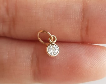 May include: A small gold charm with a clear round gemstone.