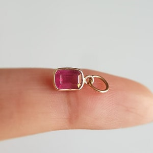 Peut inclure: Un petit charme en or avec une pierre précieuse rectangulaire rose. Le charme a une petite boucle pour l'attacher à un collier ou un bracelet.
