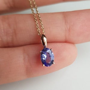 Op de afbeelding: Een delicate gouden ketting met een hanger met een grote ovale paarse edelsteen.