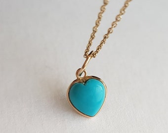 May include: A gold-colored necklace with a turquoise heart-shaped pendant. The pendant is a vibrant, solid turquoise color, set in a gold-colored bezel. The chain is delicate and gold-colored, with a simple clasp.