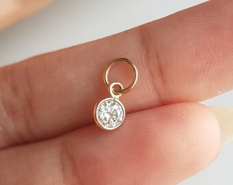 May include: A small gold charm with a clear round gemstone. The charm has a small loop for attaching to a necklace or bracelet.