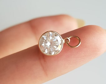 May include: A gold charm with a clear round crystal stone. The charm has a small loop for attaching to a necklace or bracelet.