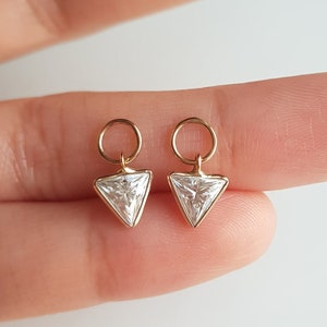 Könnte beinhalten: Ein Paar goldene Ohrringe mit einem dreieckigen, klaren Edelstein-Anhänger. Jeder Ohrring hat einen kleinen goldenen Ring.