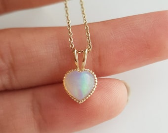Puede incluir: Un delicado collar de cadena de oro con un pequeño colgante de ópalo en forma de corazón. El ópalo es iridiscente con tonos de blanco, azul y verde.