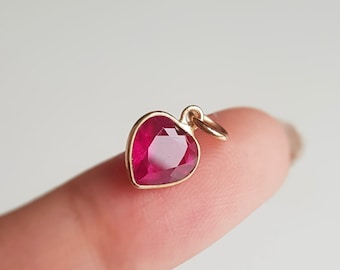 May include: A gold heart-shaped pendant with a red gemstone.