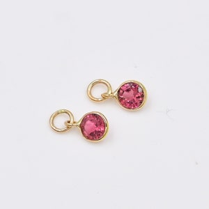May include: Two gold charms with pink gemstones. Each charm has a small loop for attaching to a necklace or bracelet.