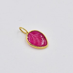 May include: A pink gemstone pendant with a gold leaf design. The pendant is shaped like a teardrop and has a gold bail.