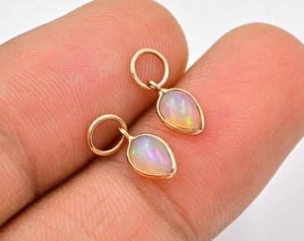 May include: A pair of gold teardrop earrings with opal stones. The earrings are on a finger.