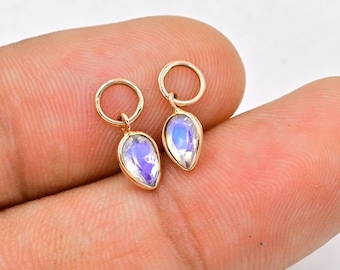 May include: A pair of gold-toned earrings with a teardrop-shaped moonstone charm. The charms have an iridescent finish.