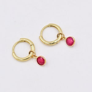 May include: A pair of gold hoop earrings with a dangling red gemstone. The earrings are simple and elegant.
