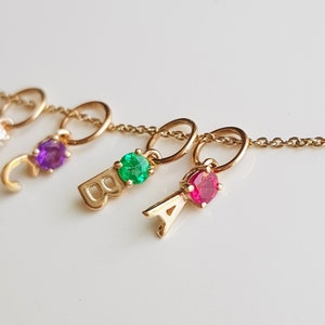 May include: Gold necklace with letter charms and colorful gemstones. The charms include the letters A, B, and C, with a purple, green, and red gemstone on each charm.