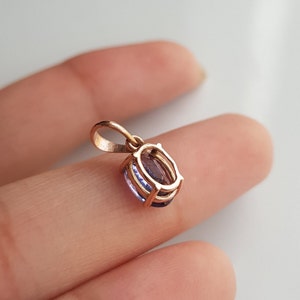 May include: A gold pendant with a purple oval gemstone set in a bezel setting. The pendant has a bail for attaching to a chain.