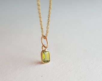 May include: A gold chain necklace with a small, rectangular pendant featuring a green gemstone.