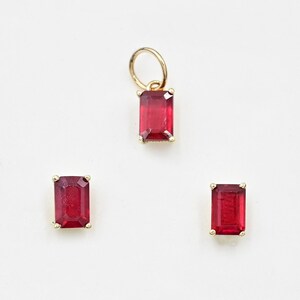 May include: A set of three gold earrings with red gemstone accents. The earrings feature a rectangular emerald cut gemstone.
