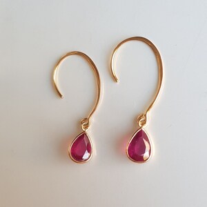 May include: A pair of gold earrings with teardrop-shaped ruby red stones.