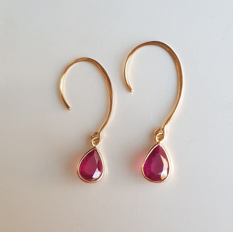 May include: A pair of gold earrings with teardrop-shaped ruby red stones.