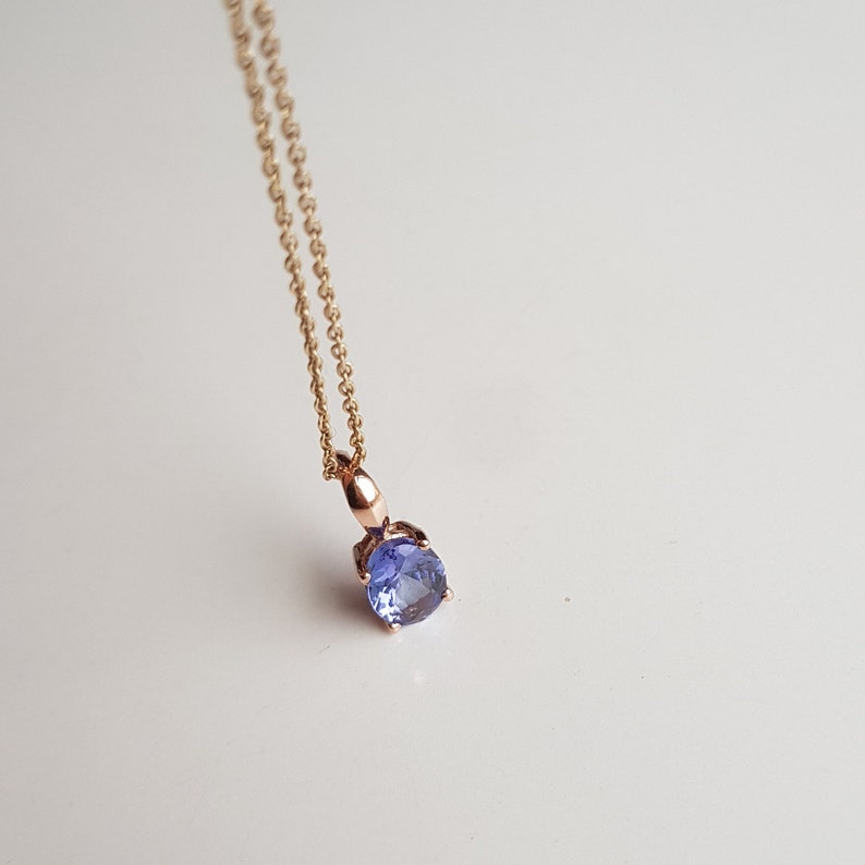 Op de afbeelding: Een delicate gouden ketting met een klein rond hanger met een blauwe edelsteen.