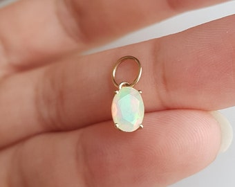Puede incluir: Un charm de oro con una piedra preciosa de ópalo blanco. El ópalo tiene forma ovalada y un corte facetado. El charm tiene un pequeño bucle en la parte superior para sujetarlo a un collar o pulsera.