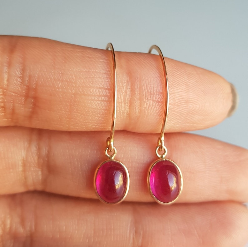 May include: A pair of gold hoop earrings with oval-shaped red gemstones. The earrings are simple and elegant.