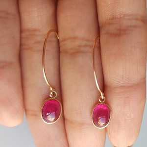 May include: A pair of gold dangle earrings with oval-shaped red gemstones.