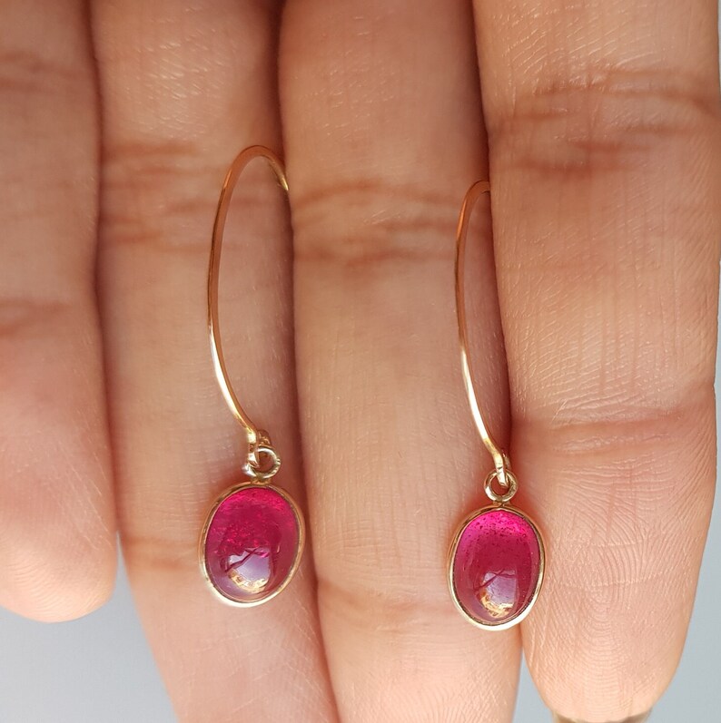 May include: A pair of gold dangle earrings with oval-shaped red gemstones.