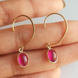 May include: A pair of gold hoop earrings with a dangling oval-shaped pink gemstone.