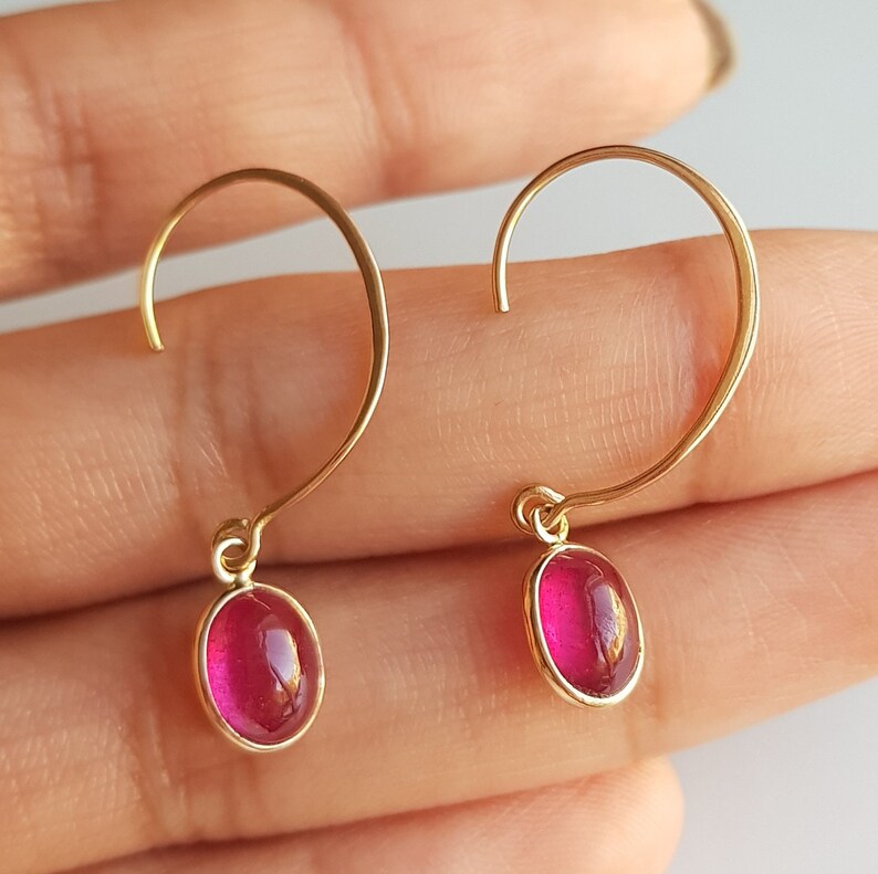 May include: A pair of gold hoop earrings with a dangling oval-shaped pink gemstone.