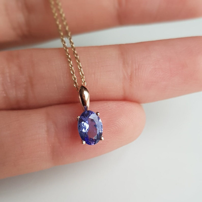 Op de afbeelding: Een delicate gouden ketting met een hanger met een grote ovale paarse edelsteen.