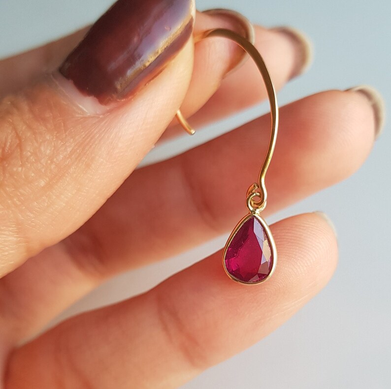 May include: Gold earring with a teardrop-shaped red gemstone.