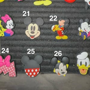 May include: A collection of colorful cartoon character charms, including Mickey Mouse, Minnie Mouse, and Donald Duck. The charms feature various designs and colors, perfect for personalizing accessories.