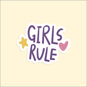 May include: Purple sticker with the text "GIRLS RULE" in white outlined lettering. A yellow star is to the left of the text and a pink heart is to the right.