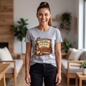 Puede incluir: Una camiseta gris jaspeado con un gráfico de una taza de café humeante y una lista de tareas. El texto dice: Because some days my To do list needs a TRIGGER WARNING. El diseño incluye tintas de color marrón, beige y negro.